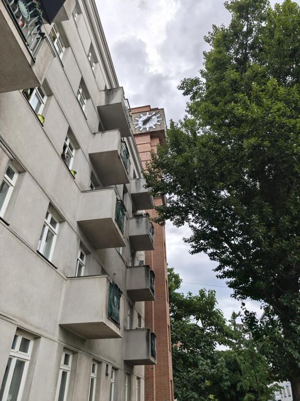 Ein Wohnhaus mit hervortretenden Balkonen und einer großen Uhr an der Fassade.
