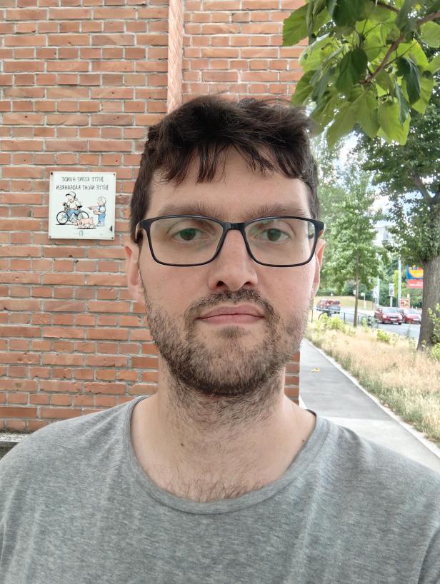 Ein Mann mit Brille steht vor einer Backsteinmauer.