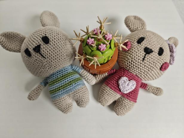 Zwei gehäkelte Hasen stehen neben einem Lego-Kaktus mit rosa Blüten.