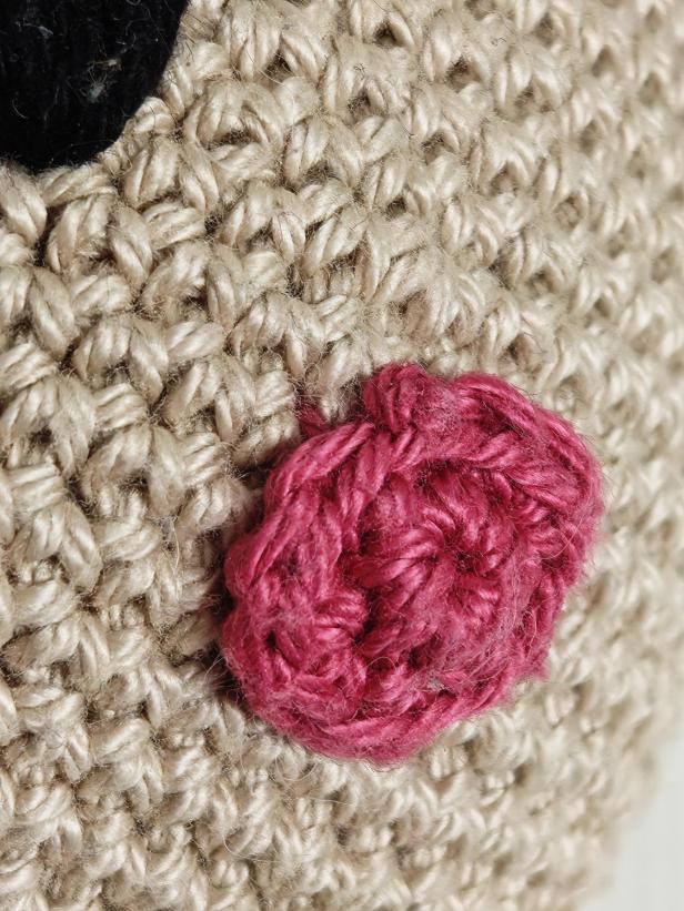 Detailaufnahme eines gehäkelten Stofftiers mit rosa Nase und schwarzem Auge.