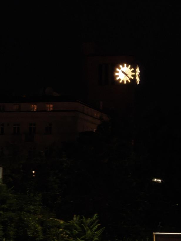 Eine beleuchtete Uhr an einem Gebäude in der Nacht.