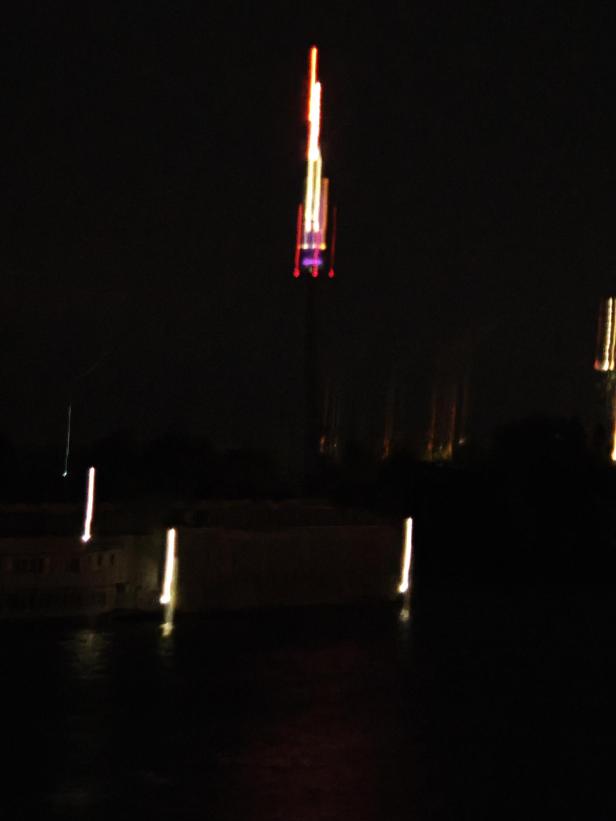 Ein verschwommenes Nachtfoto zeigt Lichter, die sich im Wasser spiegeln.