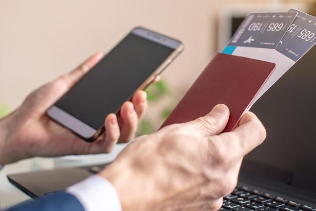 Es ist ratsam, wichtige Dokumente wie Reisepass oder Flugtickets als Kopie am Handy zu speichern. Man holding airline ticket and phone in hand buying on the Internet using a laptop. Purchasing and booking online