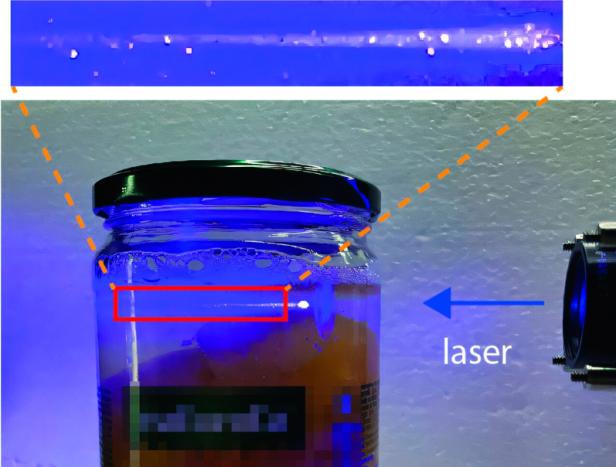 In diesem Laser-Barcode im Pfirsich-Mus haben die Forscherinnen und Forscher ein Datum gespeichert. Ein Schraubglas wird von einem bläulichen Laser angestrahlt.