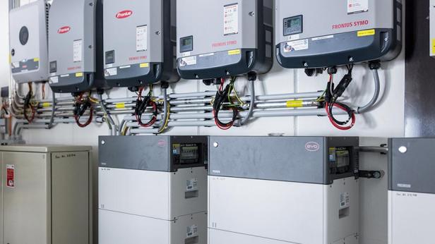 Mehrere Fronius Symo Wechselrichter und BYD Batteriespeicher sind an einer Wand montiert.