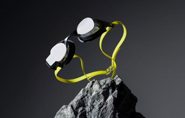 Eine Schwimmbrille mit gelbem Band liegt auf einem grauen Stein.