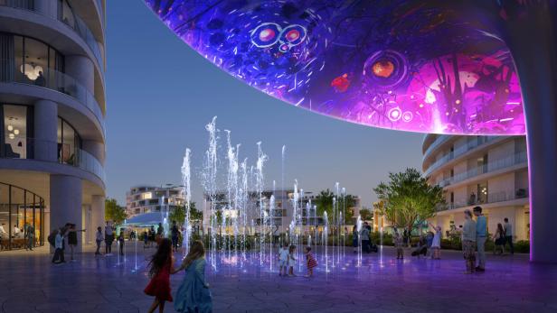 Kinder spielen an einem Brunnenplatz unter einer großen, beleuchteten Struktur in einer Stadt.