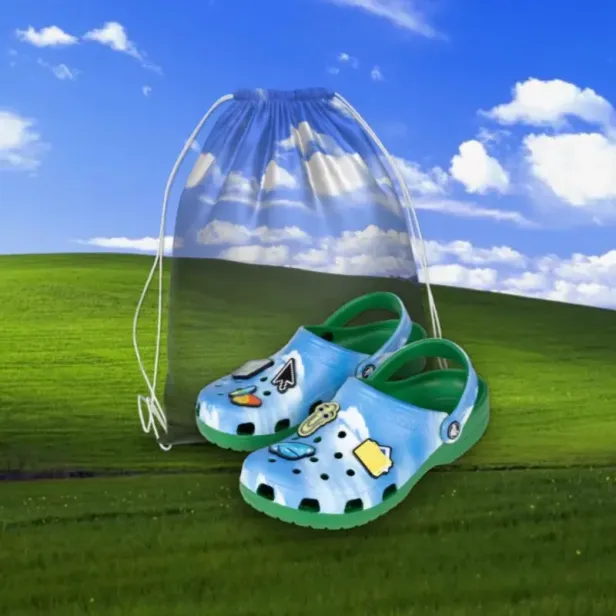 Blaue Crocs im Windows XP-Stil mit Ansteckern vor einem passenden Turnbeutel.