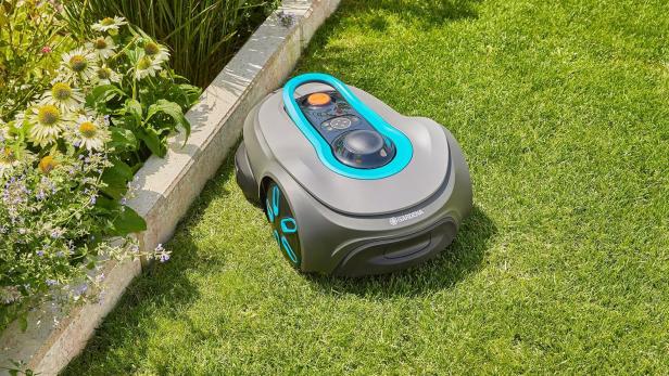 Ein grauer Gardena Mähroboter steht auf einem grünen Rasen.