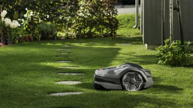 Ein Rasenmähroboter steht auf einem grünen Rasen mit Trittsteinen.