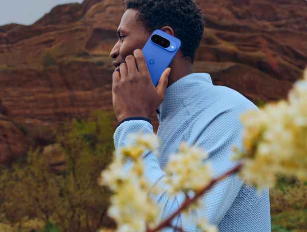 Ein Mann telefoniert mit einem blauen Google Pixel vor einer Felslandschaft.