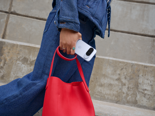 Eine Person in Jeanskleidung hält ein Google Pixel-Smartphone und eine rote Handtasche.