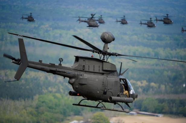 Ein OH-58D Kiowa Warrior Hubschrauber im Flug, mit weiteren Hubschraubern im Hintergrund.