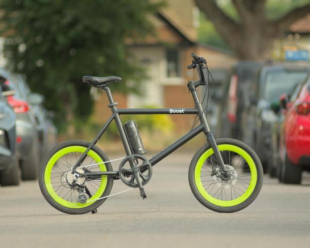 Ein schwarzes „Boost“-Fahrrad mit grünen Felgen steht auf einer Straße.