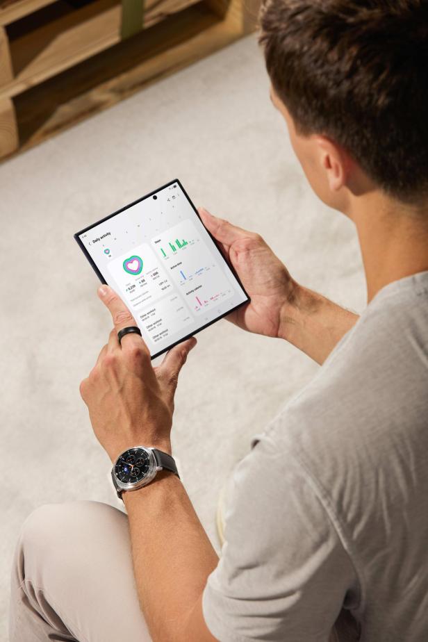 Ein Mann betrachtet seine täglichen Aktivitätsdaten auf einem Tablet, mit einer Smartwatch am Handgelenk.