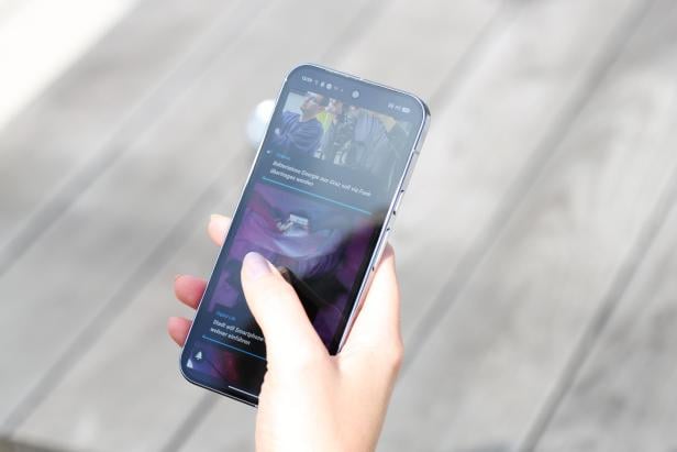 Eine Hand hält ein Smartphone mit Nachrichten über batterielose Energie und Smartphone-Wohnungen.