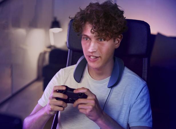 Ein junger Mann spielt mit einem Controller und einem Nackenlautsprecher von Panasonic SC-GN01.