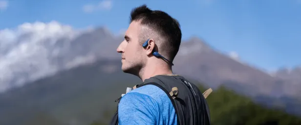 Ein Mann mit Knochenschallkopfhörern von Shokz vor einer Bergkulisse.