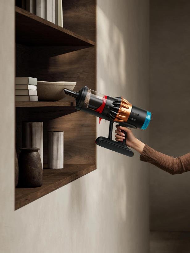 Eine Person benutzt einen Akku-Staubsauger, um ein Regal zu reinigen.