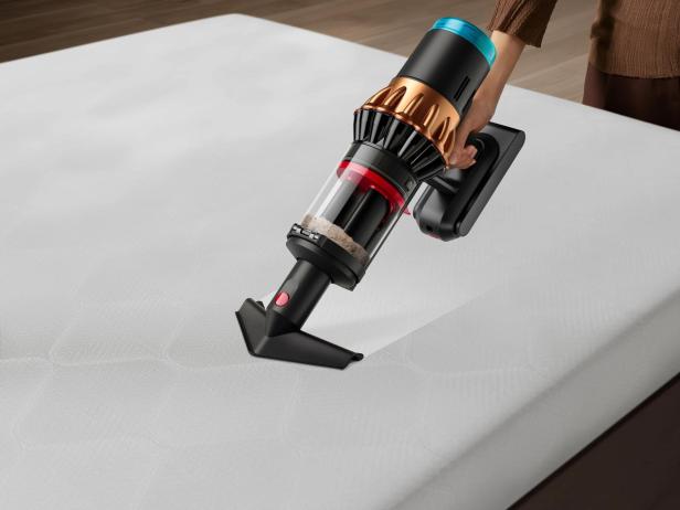 Eine Person saugt eine weiße Matratze mit einem Akku-Staubsauger ab.