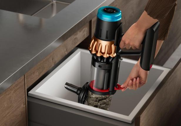 Eine Hand entleert einen Dyson V16 Staubsauger in ein Waschbecken.