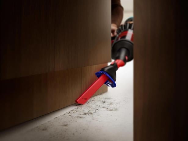 Ein Staubsauger mit Bürstenaufsatz reinigt den Boden entlang einer dunklen Holztür.