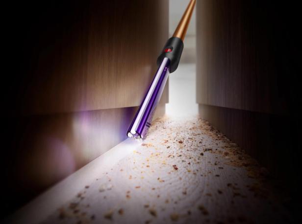 Ein Staubsauger mit Licht reinigt Krümel entlang einer dunklen Fußleiste.