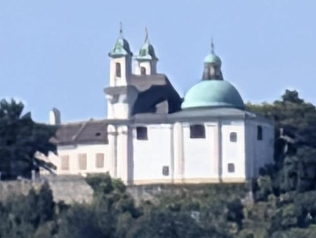 Eine weiße Kirche mit einem grünen Kuppeldach steht auf einem Hügel.