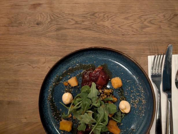 Ein Teller mit einem Gericht aus Fleisch, Gemüse und Soße auf einem Holztisch.