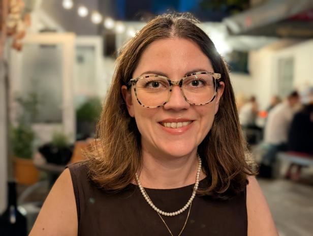 Eine lächelnde Frau mit Brille und Perlenkette in einem Restaurant.