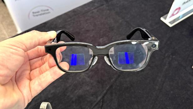 Eine Hand hält die Rokid-Brille mit blauen Anzeigen in den Gläsern.