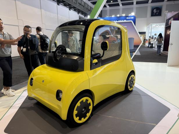 Ein gelbes elektrisches Microcar von Astraux steht auf einer Messe.