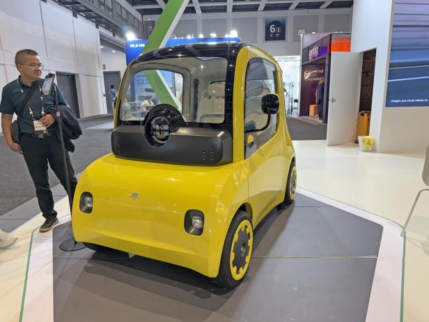 Ein gelbes elektrisches Microcar von Astraux steht auf einer Messe.