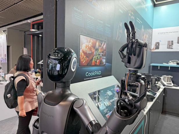 Der Küchenroboter Robbyant steht auf einer Messe neben einem Bildschirm mit Rezepten.