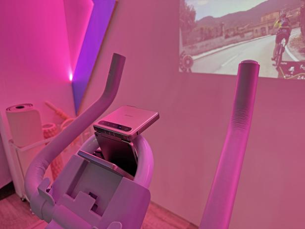 Ein Mini-Beamer der Marke Aurzen ist an einem pinken Heimtrainer befestigt.
