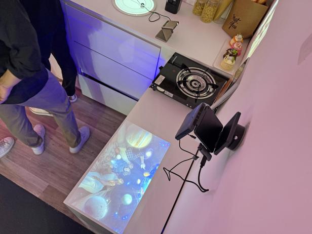 Ein Mini-Beamer projiziert ein Bild mit Planeten und Menschen auf eine Tischoberfläche.