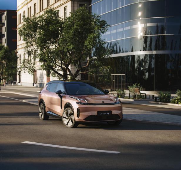 Ein rosafarbener Lynk & Co 08 steht auf einer Straße in der Stadt.