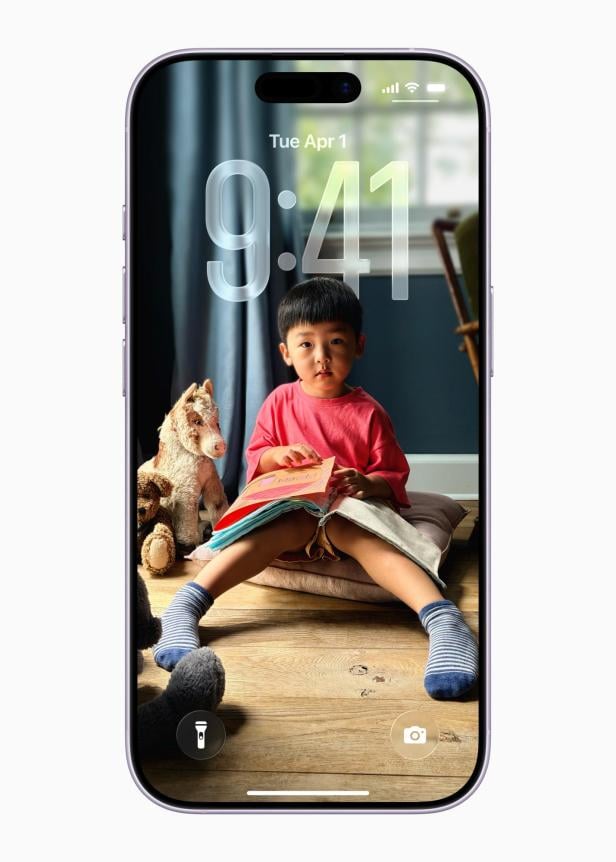 Ein Kind sitzt mit einem Buch und Stofftieren auf einem Kissen vor dem Bildschirm eines iPhones.