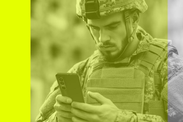 Ein Soldat in Uniform und Helm benutzt ein Smartphone.
