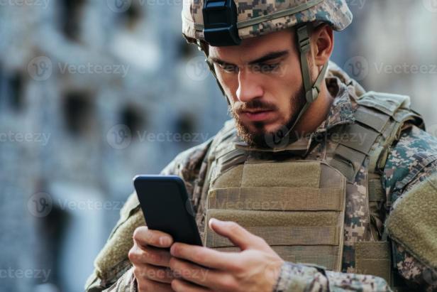 Ein Soldat in Uniform und Helm blickt auf sein Smartphone.
