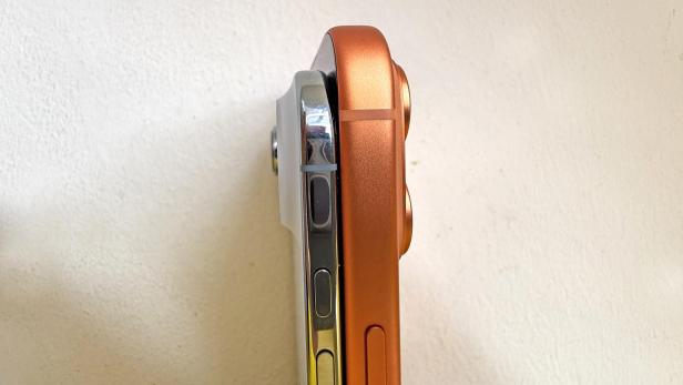 Zwei iPhones stehen nebeneinander, eines silberfarben und eines orangefarben.