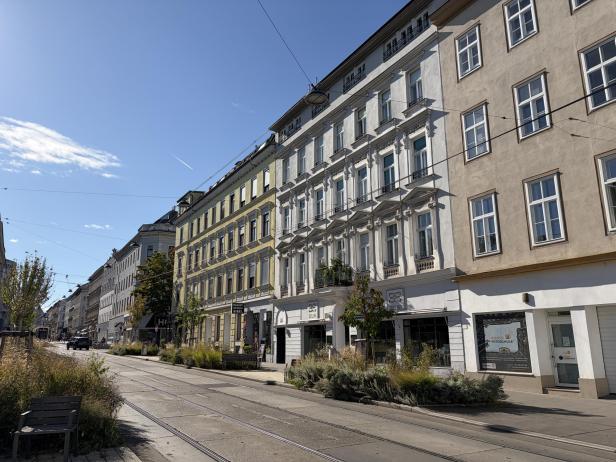 Straßenansicht mit Wohnhäusern und Straßenbahnschienen in Wien.