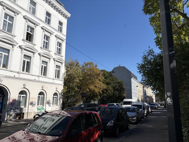 Eine Straße mit geparkten Autos und einem weißen Gebäude mit Graffiti im Vordergrund.
