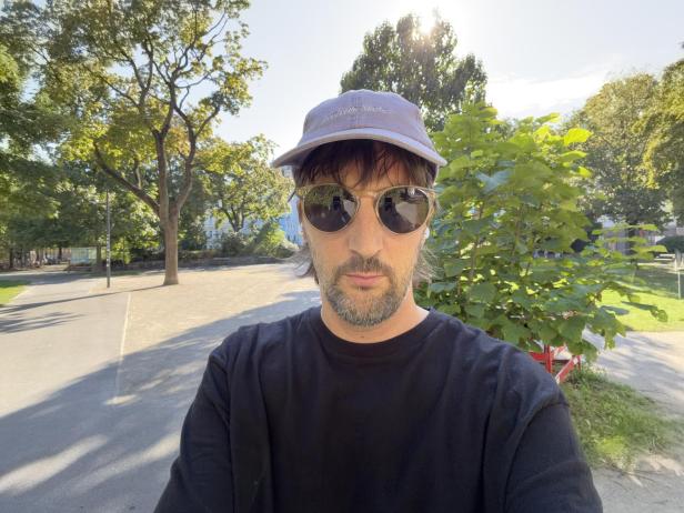 Ein Mann mit Sonnenbrille und Kappe im Park macht ein Selfie.