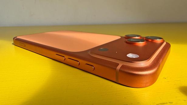 Ein orangefarbenes iPhone 17 Pro Max liegt auf einem gelben Tisch.