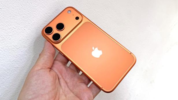 Ein orangefarbenes iPhone 17 Pro Max wird in der Hand gehalten.