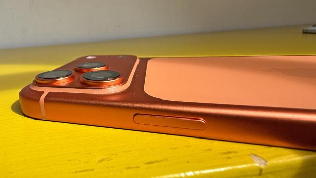 Ein orangefarbenes iPhone 17 Pro Max liegt auf einem gelben Tisch.