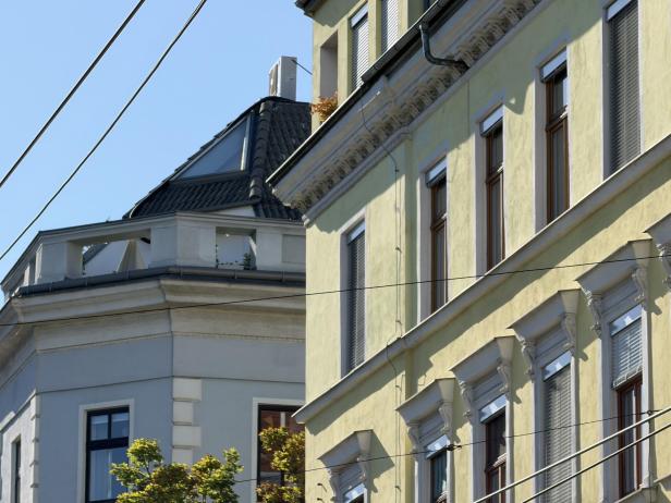 Die Fassaden zweier Wohnhäuser mit unterschiedlicher Architektur unter blauem Himmel.