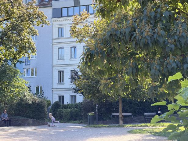 Ein Mädchen fährt mit einem Roller durch einen Park.