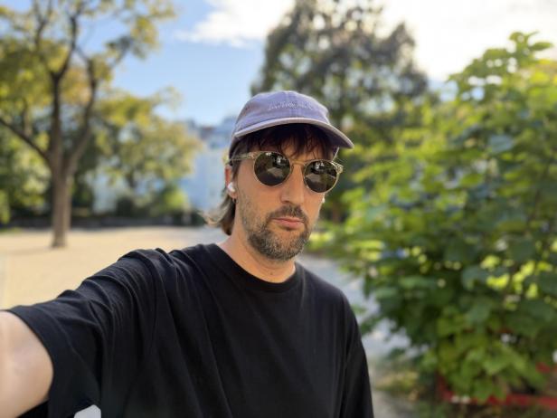 Ein Mann mit Sonnenbrille und Kappe macht ein Selfie im Park.